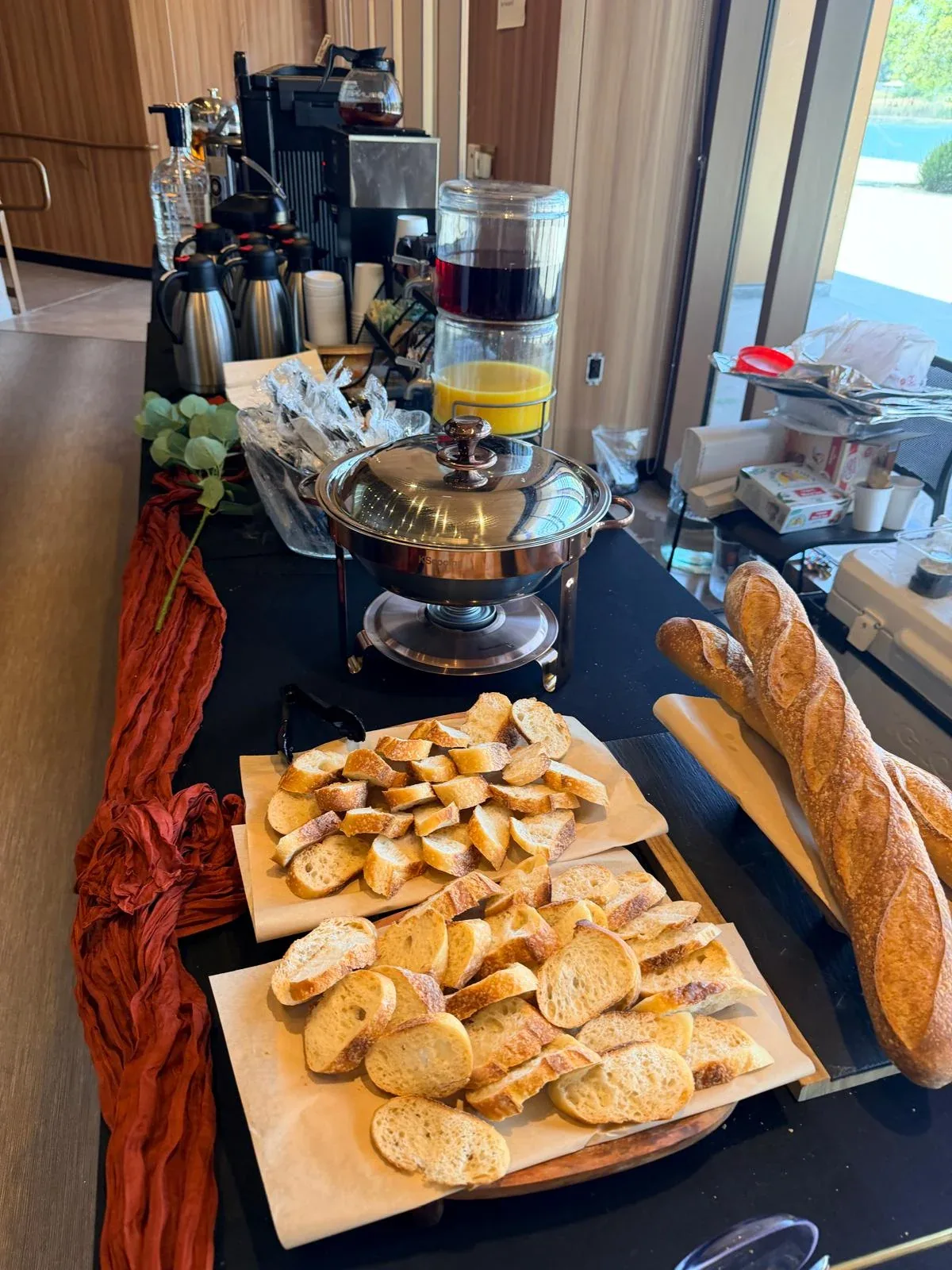 Crisp crust artisanal French baguettes sliced on wood board next to stainless lunch chafers