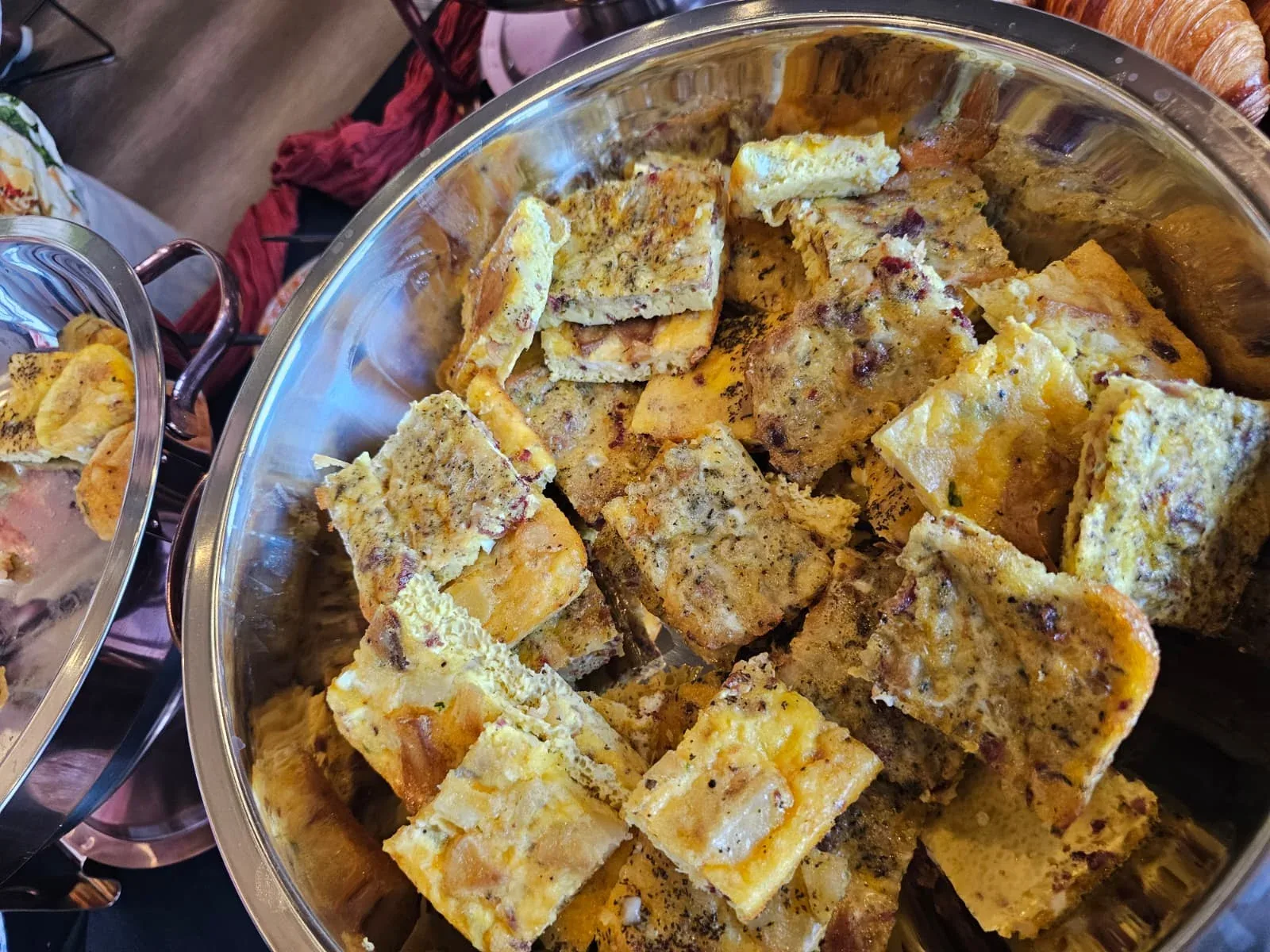Golden baked cheddar and Yukon potato frittata squares kept warm in stainless round chafing dish