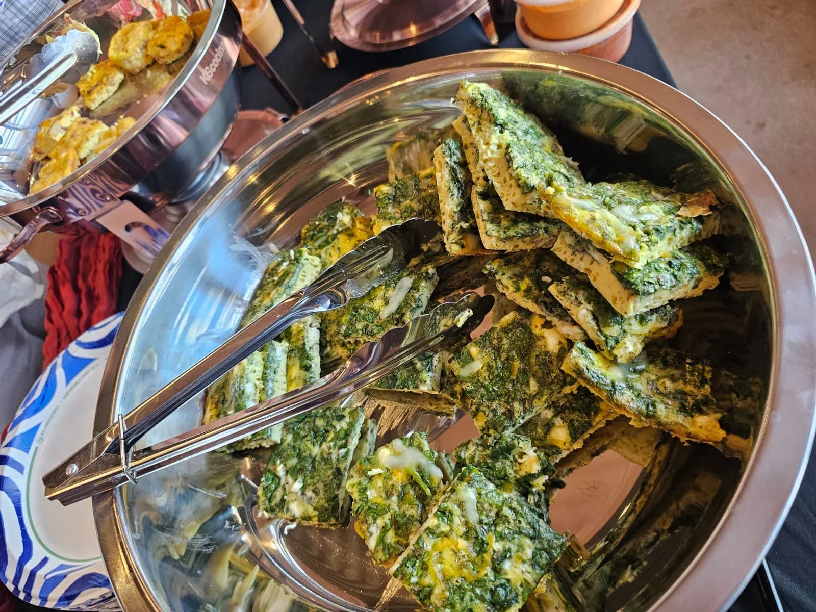 Fresh spinach and herb egg frittata slices served hot with stainless serving tongs